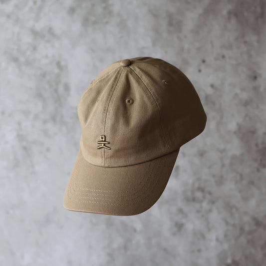 Framsida. Sand beige 6-panel keps med beige broderad logotyp. 100% organisk bomull. Justerbar rem. One size. Ostrukturerad front.